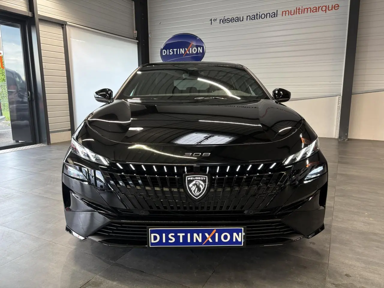 Vue avant d'une Peugeot 308 GT noire métallisée avec calandre noire brillante et logo lion lumineux.