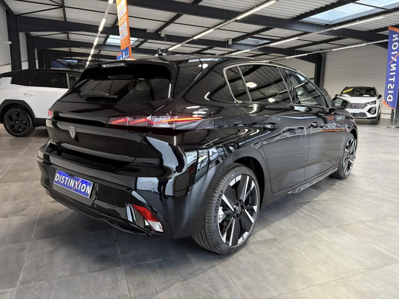 Vue 3/4 arrière droite d'une Peugeot 308 GT noire métallisée avec jantes alliage bi-tons et feux arrière LED 3 griffes.