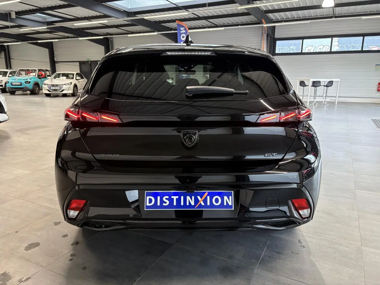 Vue arrière d’une Peugeot 308 GT noire métallisée avec feux arrière LED en forme de griffes, en showroom.