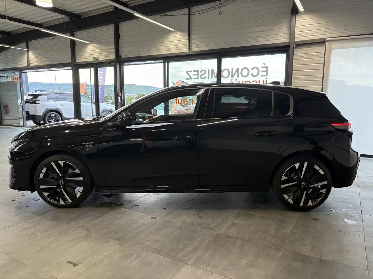 Peugeot 308 noir métallisé vue de profil côté gauche, avec jantes alliage bi-tons et blason sur aile avant.