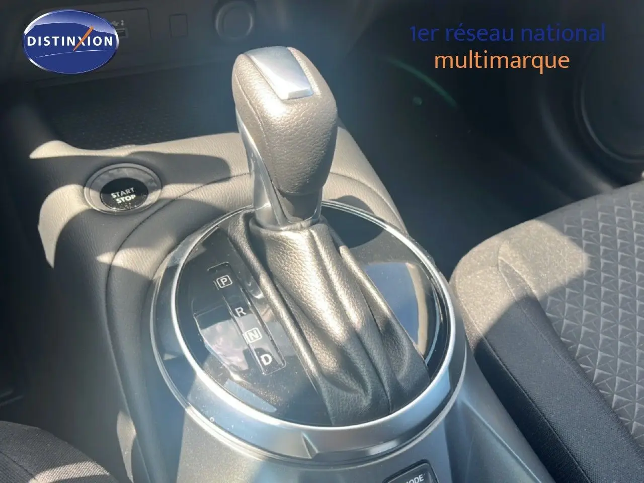Le levier de vitesses automatique noir du Nissan Juke Hybrid 2025, avec bouton start/stop et siège tissu gris visible.