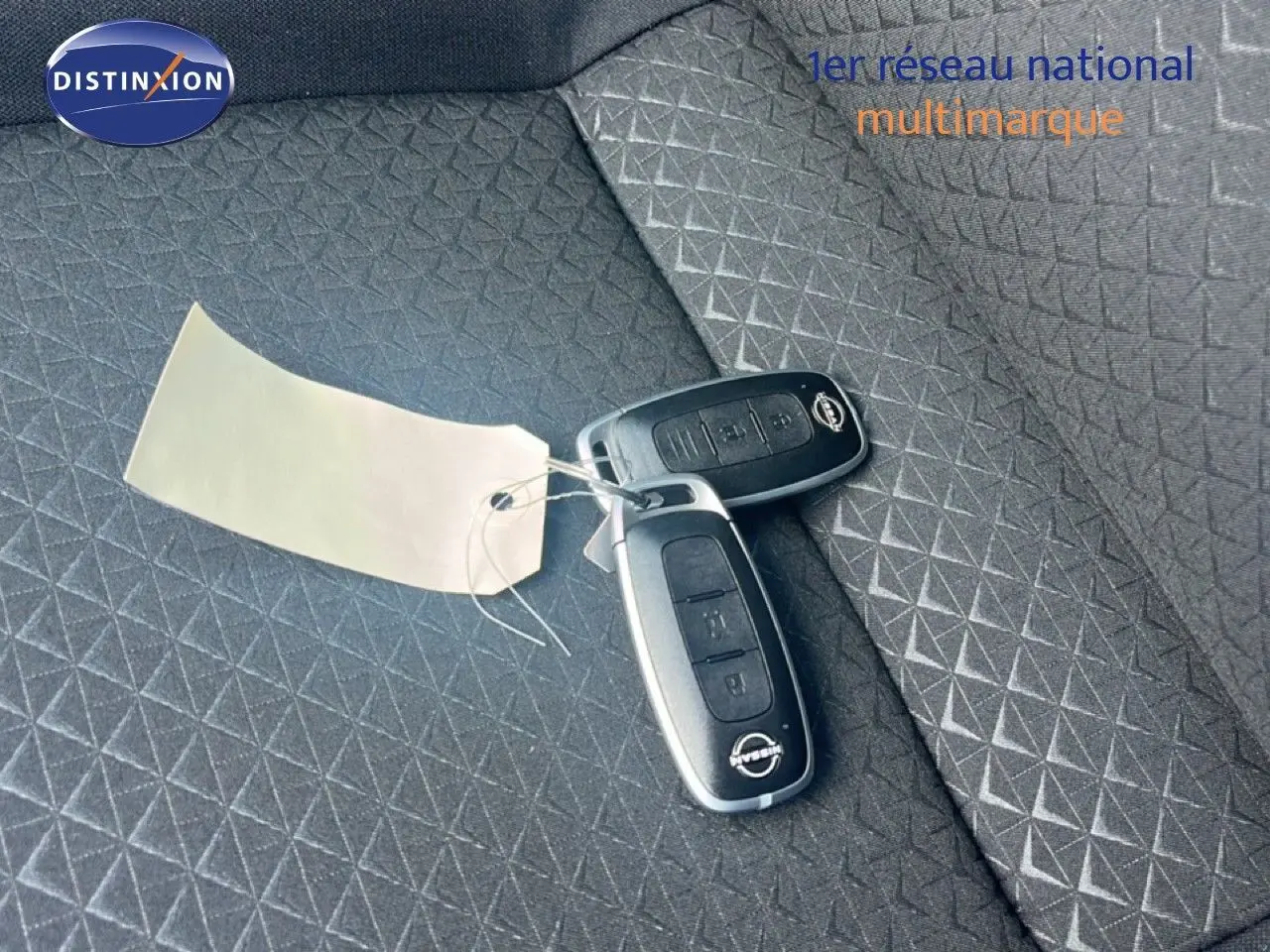 Clé de voiture Nissan posée sur un siège tissu gris à motifs géométriques, intérieur du Nissan Juke Hybrid 2025.