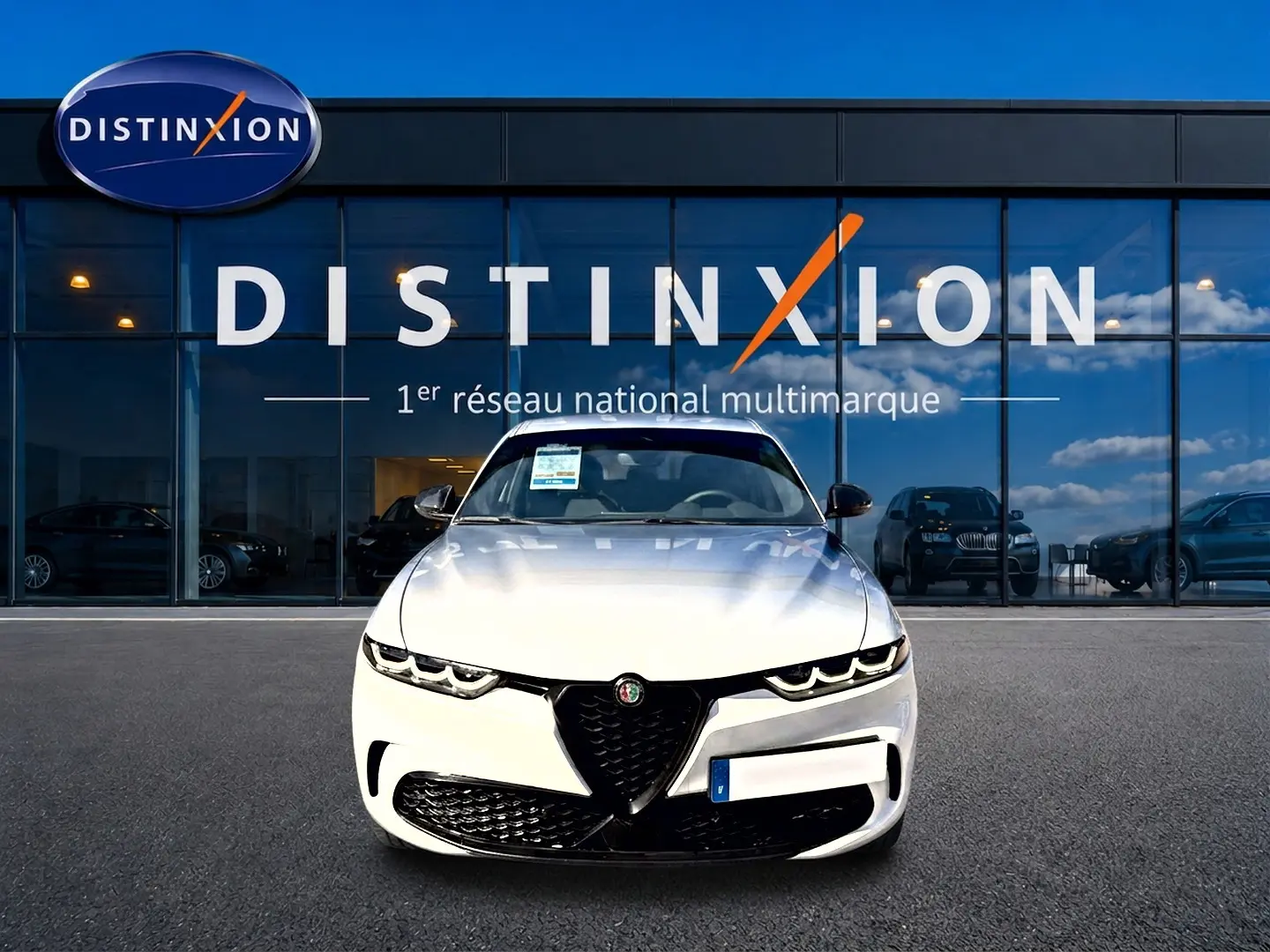 Vue frontale d'une Alfa Romeo Tonale blanche 2025 avec calandre noire et phares LED, devant une vitrine Distinxion.