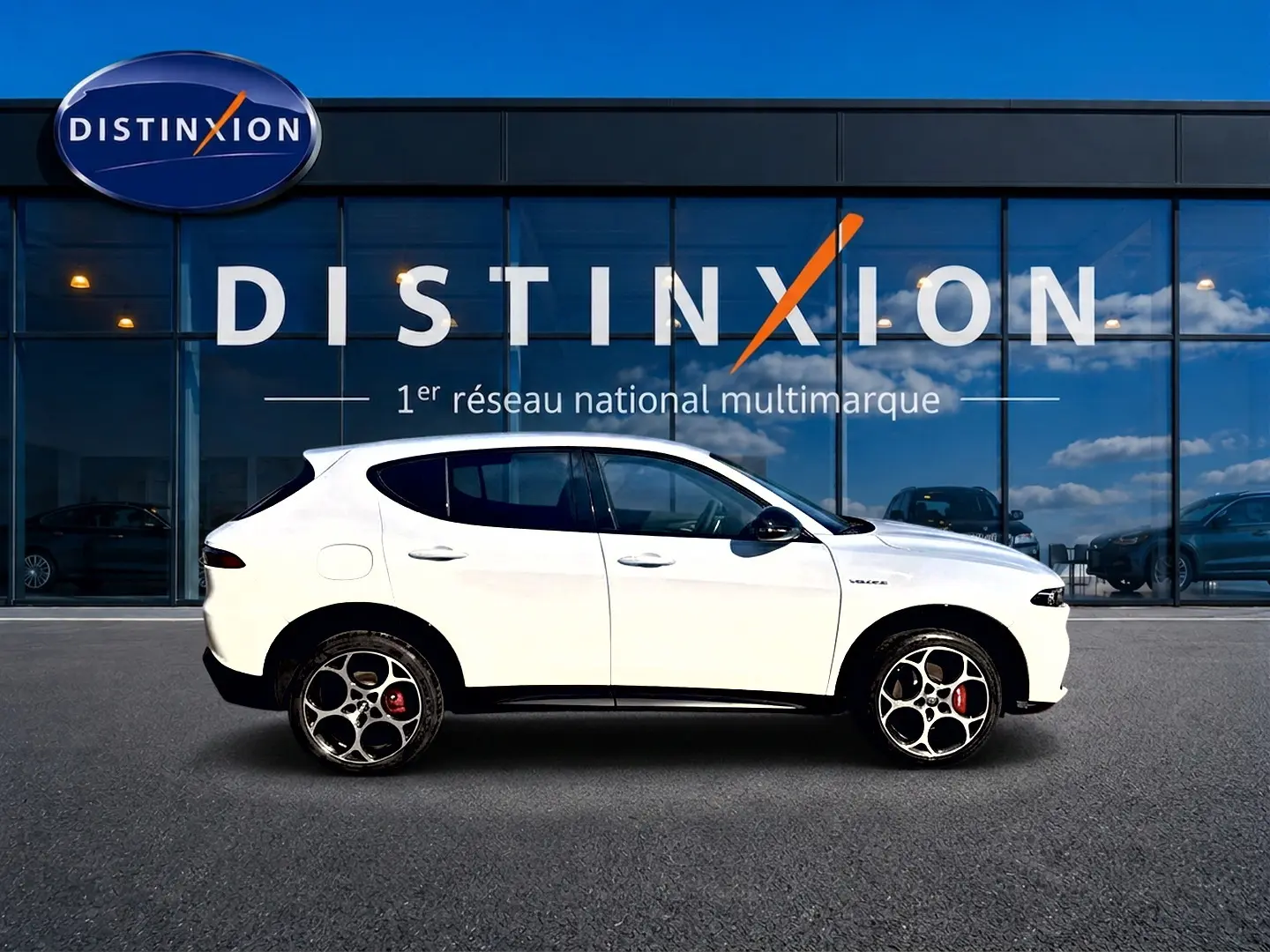 Profil droit d'un Alfa Romeo Tonale blanc 2025 avec jantes alu distinctives, devant une vitrine Distinxion.