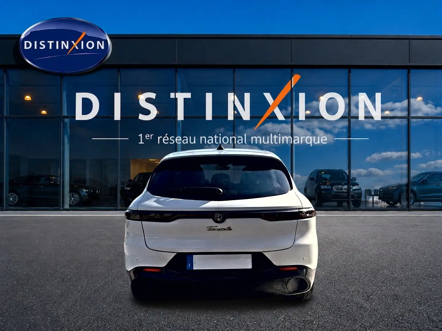 Vue arrière d'un Alfa Romeo Tonale blanc 2025, avec feux arrière LED et diffuseur noir, devant un showroom Distinxion.