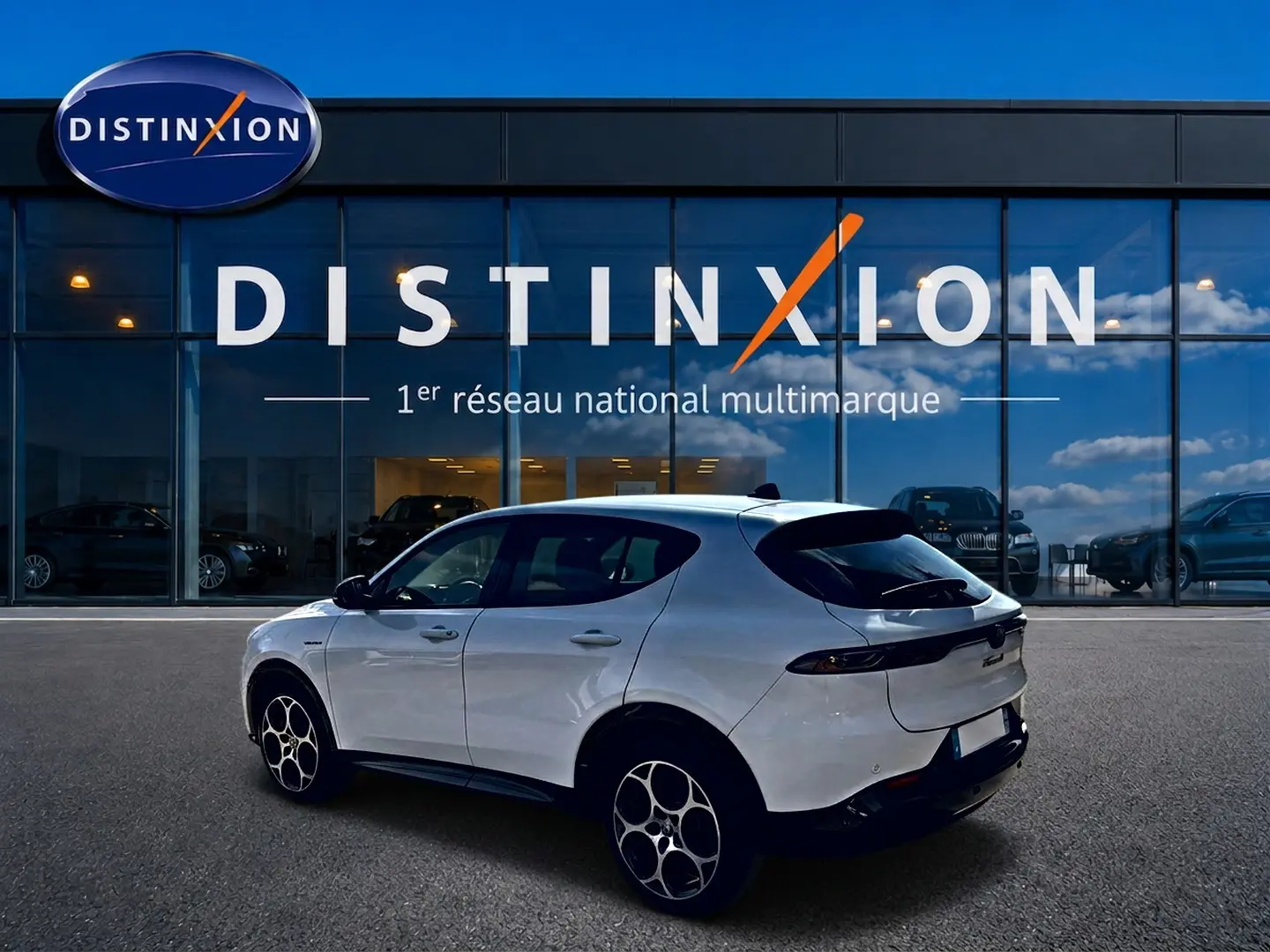 Vue 3/4 arrière droite d'une Alfa Romeo Tonale blanche 2025 avec jantes alu et becquet arrière noir devant un showroom Distinxion.