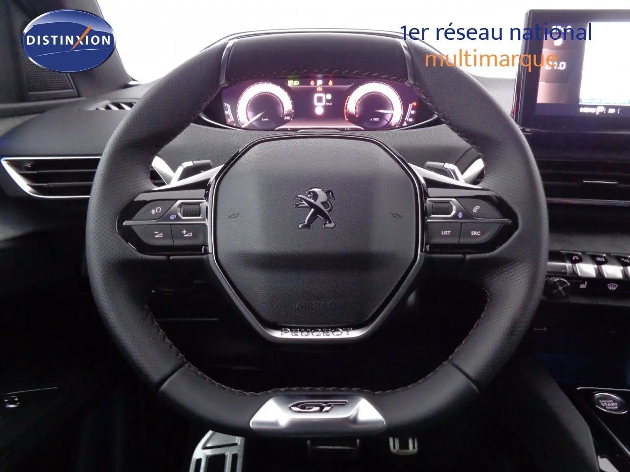 Vue rapprochée du volant GT noir perforé du Peugeot 3008 2023 avec tableau de bord numérique et écran tactile.