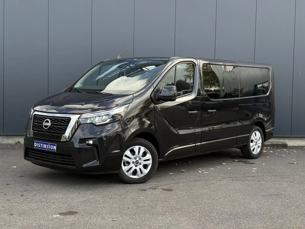 Nissan Primastar Combi noir métal en 3/4 avant droit, avec hayon vitré et vitres arrière surteintées.
