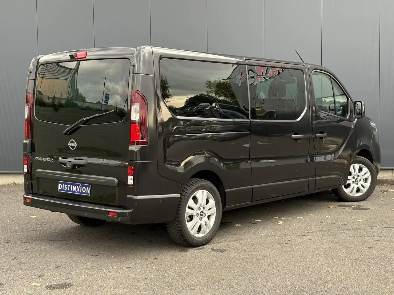 Vue 3/4 arrière droite d'un Nissan Primastar Combi noir métal avec hayon vitré et vitres latérales teintées.