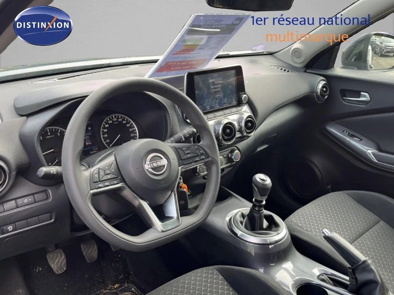 Vue intérieure côté conducteur du tableau de bord et volant du Nissan Juke 2023 en tissu noir avec écran tactile central.