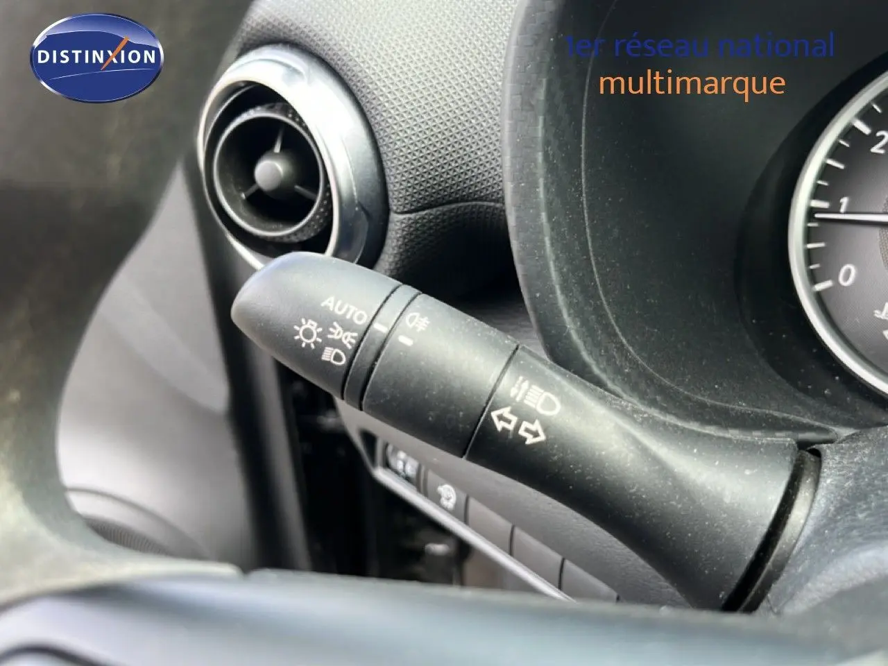 Gros plan sur le commodo d'éclairage à gauche du volant du Nissan Juke noir métal, tableau de bord partiel visible.