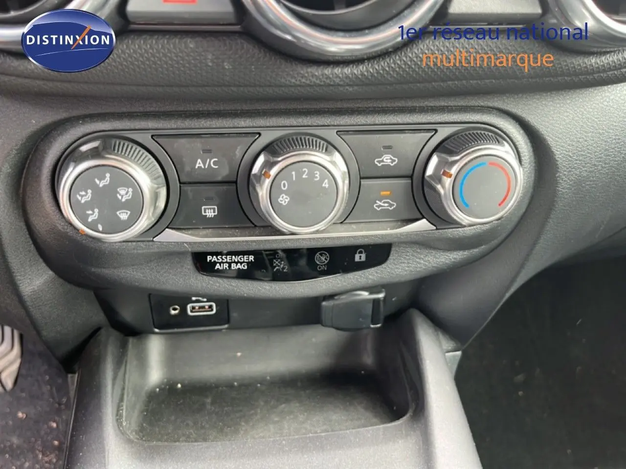 Vue rapprochée du tableau de bord du Nissan Juke noir métal 2023, montrant les commandes de climatisation et ports USB.