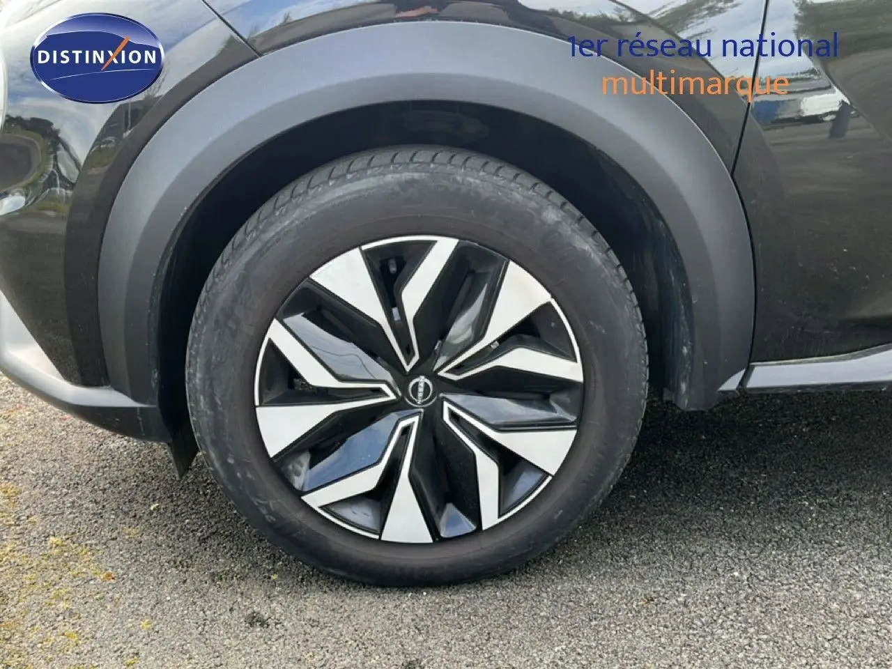 Gros plan sur la roue avant gauche du Nissan Juke noir métal 2023, mettant en valeur la jante au design moderne bicolore.