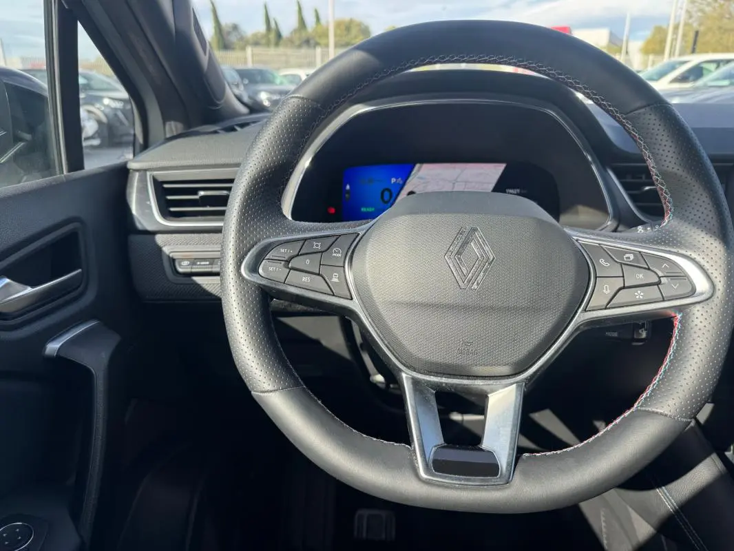 Vue intérieure centrée sur le volant noir perforé de la Renault SYMBIOZ E-Tech hybride avec tableau de bord numérique en arrière-plan.