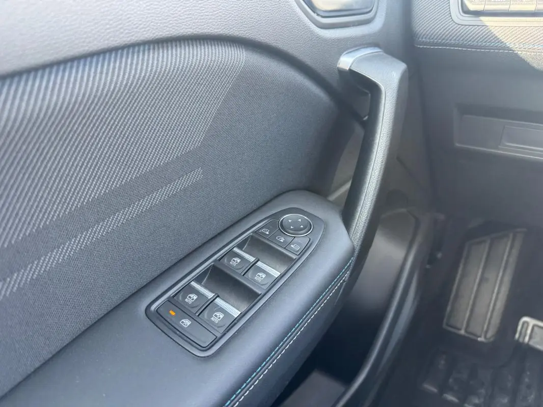 Gros plan sur la commande des vitres électriques côté gauche de la Renault SYMBIOZ gris clair, avec poignée de porte noire.