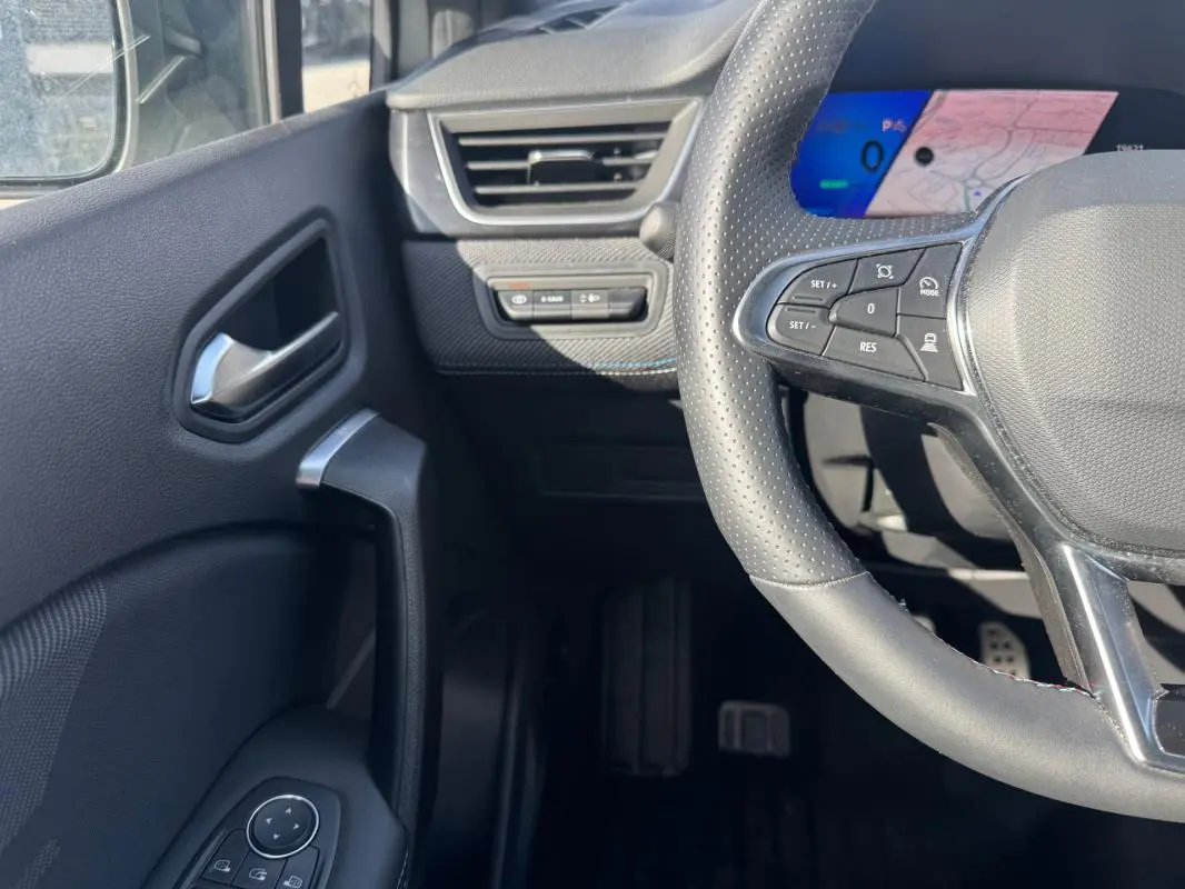 Vue intérieure côté gauche du volant perforé et du tableau de bord numérique bleu du Renault Symbioz gris clair.