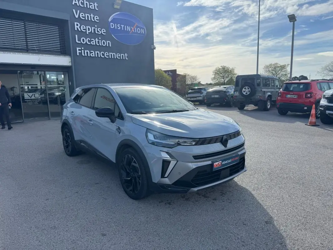 Renault Symbioz gris clair en 3/4 avant droit, jantes alliage noires de 19 pouces, devant un concessionnaire.