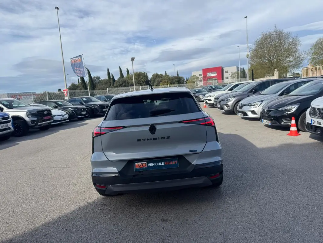 Vue arrière d'une Renault SYMBIOZ gris clair 2025 avec feux LED fins et antenne requin sur parking.
