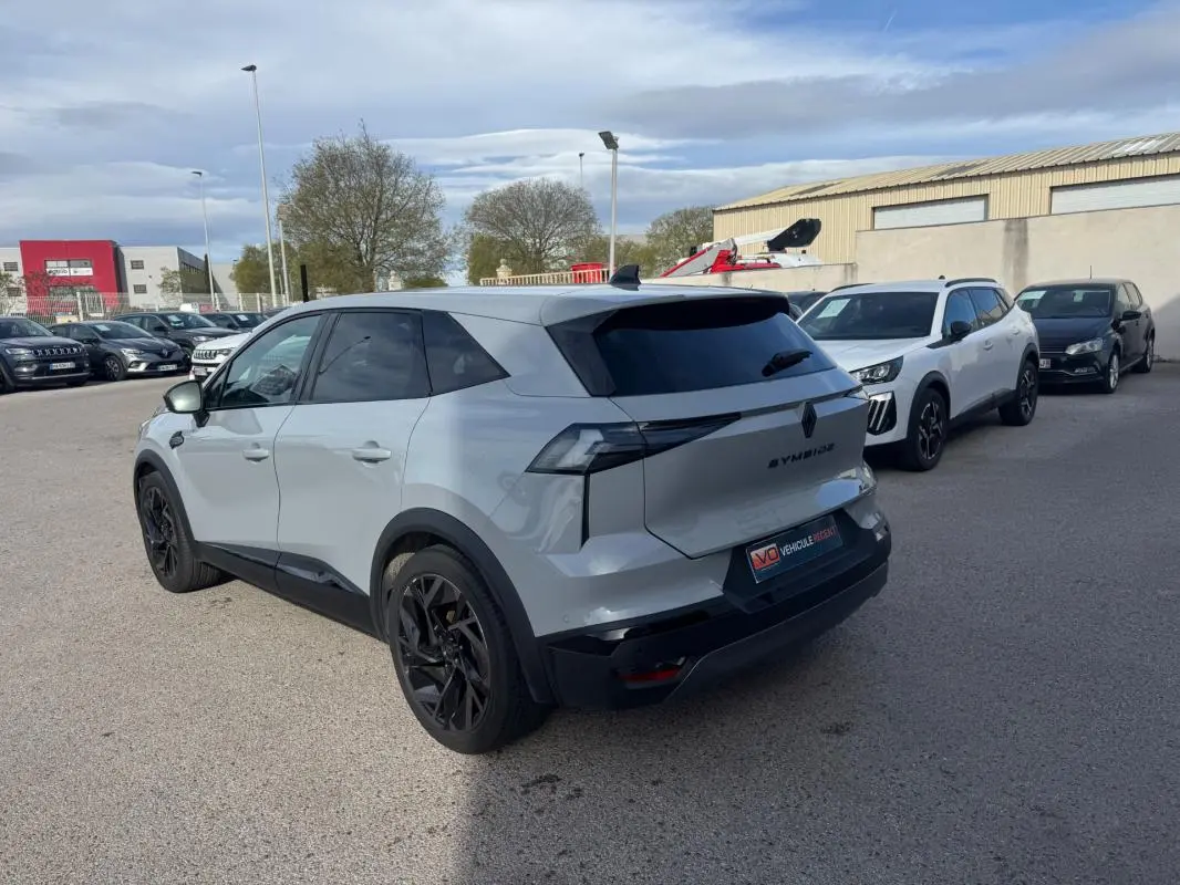 Vue 3/4 arrière droite d’un Renault SYMBIOZ gris clair avec jantes alliage noires de 19 pouces, stationné en extérieur.