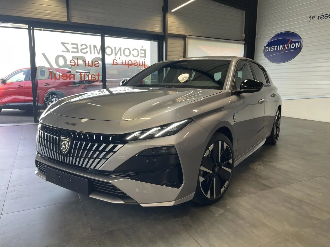 Peugeot 308 gris Artense vue 3/4 avant en intérieur, avec calandre distinctive et jantes alliage bi-tons.