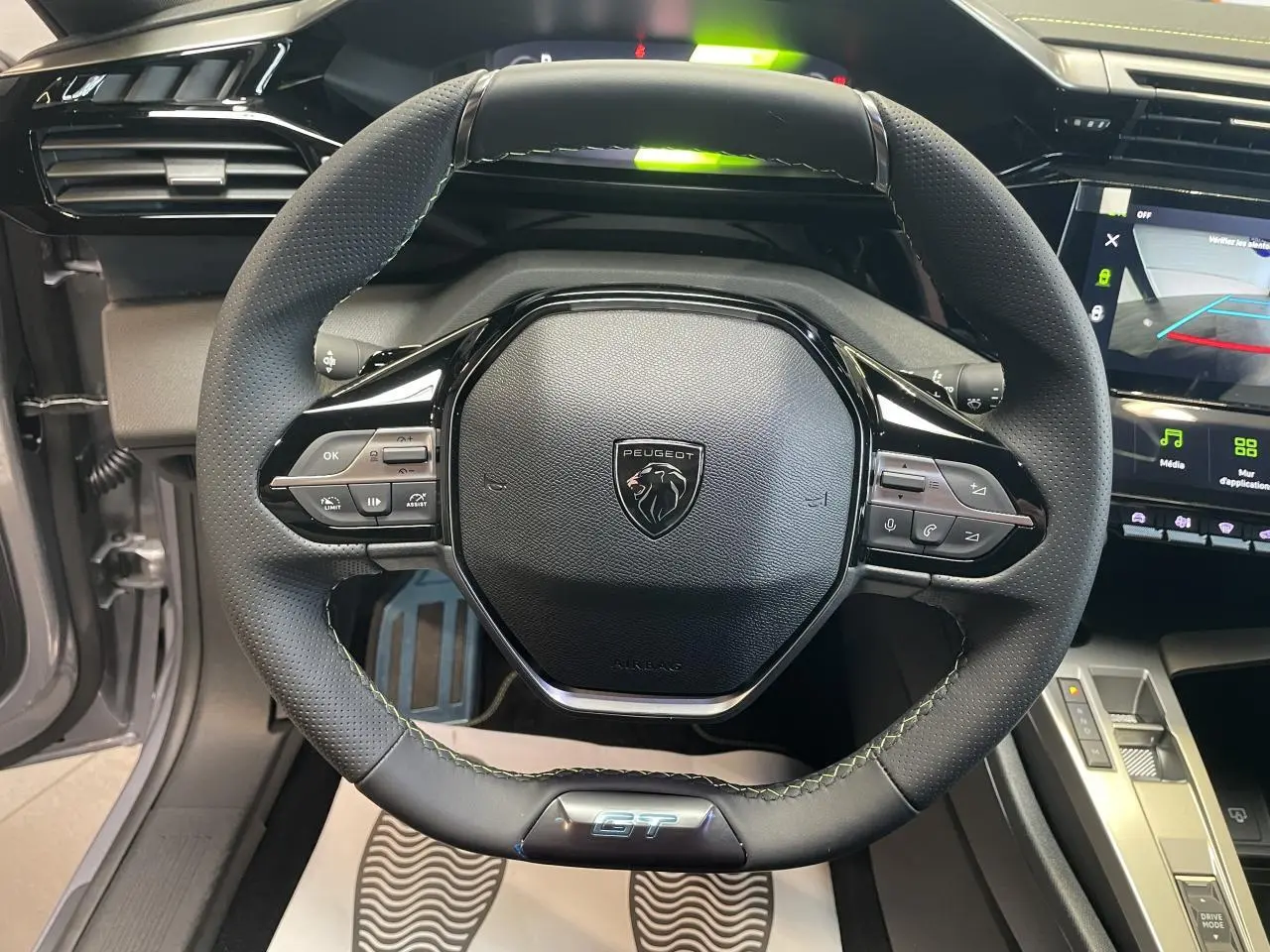 Volant compact noir de Peugeot 308 GT 2026 avec surpiqûres vert Adamite et logo GT visible en bas.