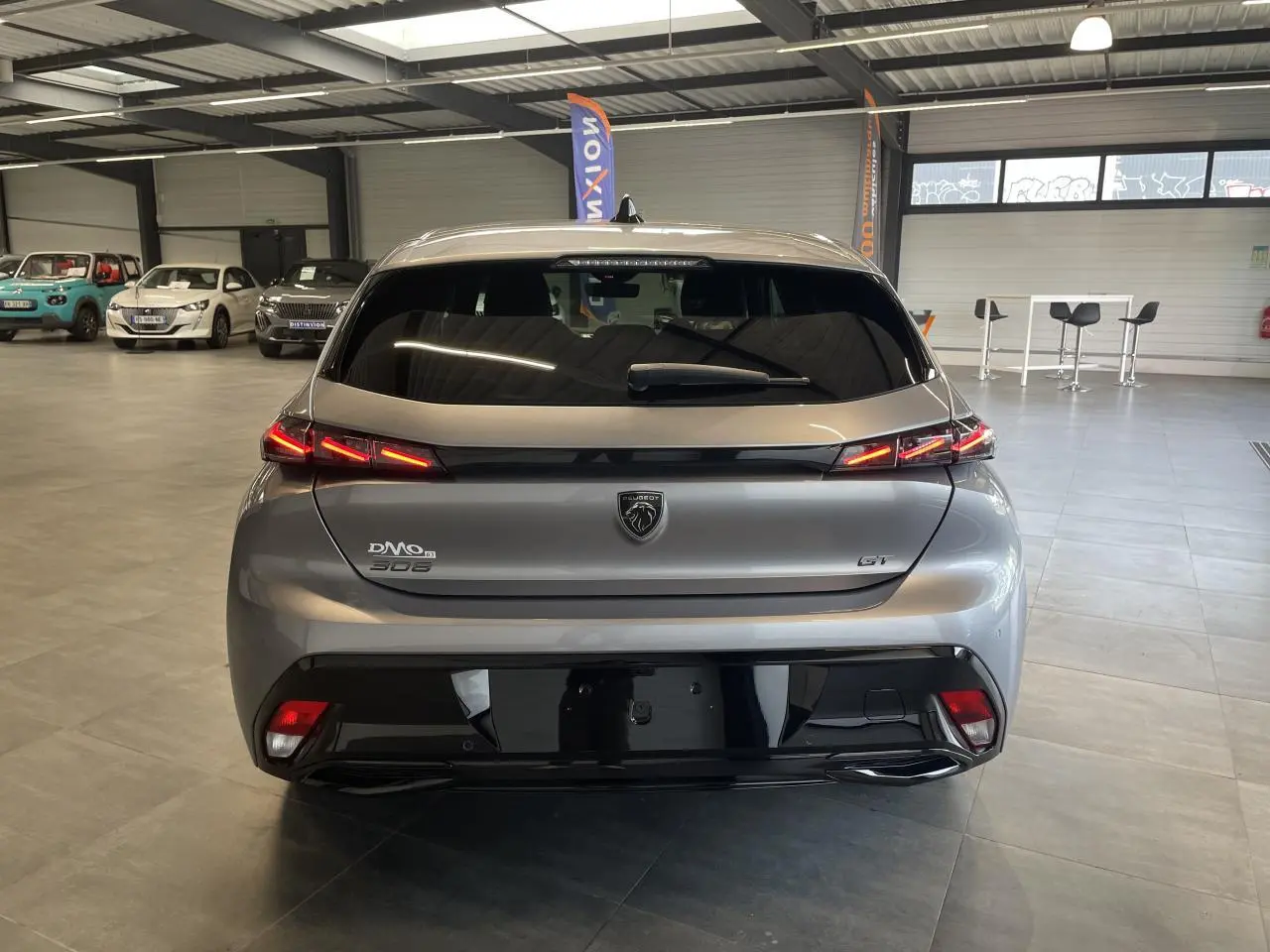 Vue arrière d'une Peugeot 308 GT gris Artense avec feux arrière LED en forme de griffes et bandeau noir brillant.