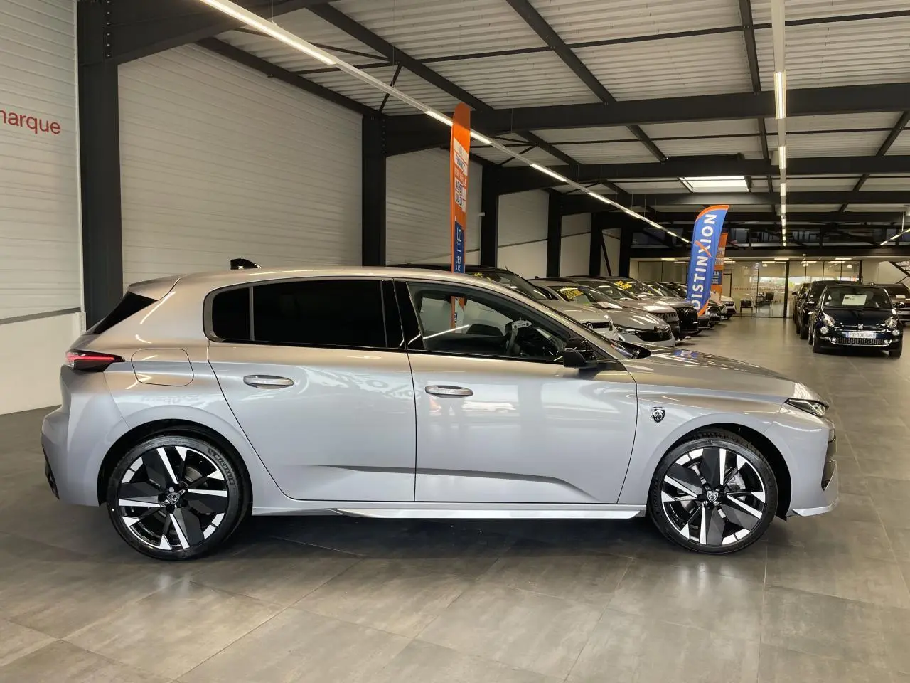 Peugeot 308 gris Artense vue de profil côté gauche, avec jantes alliage bi-tons et vitres surteintées en showroom.