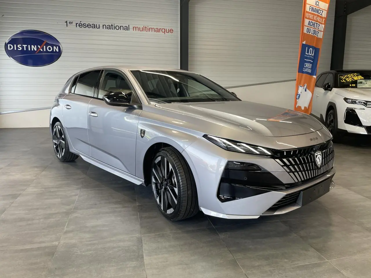 Peugeot 308 gris Artense vue 3/4 avant droit, calandre noire distinctive et jantes alliage bi-ton.