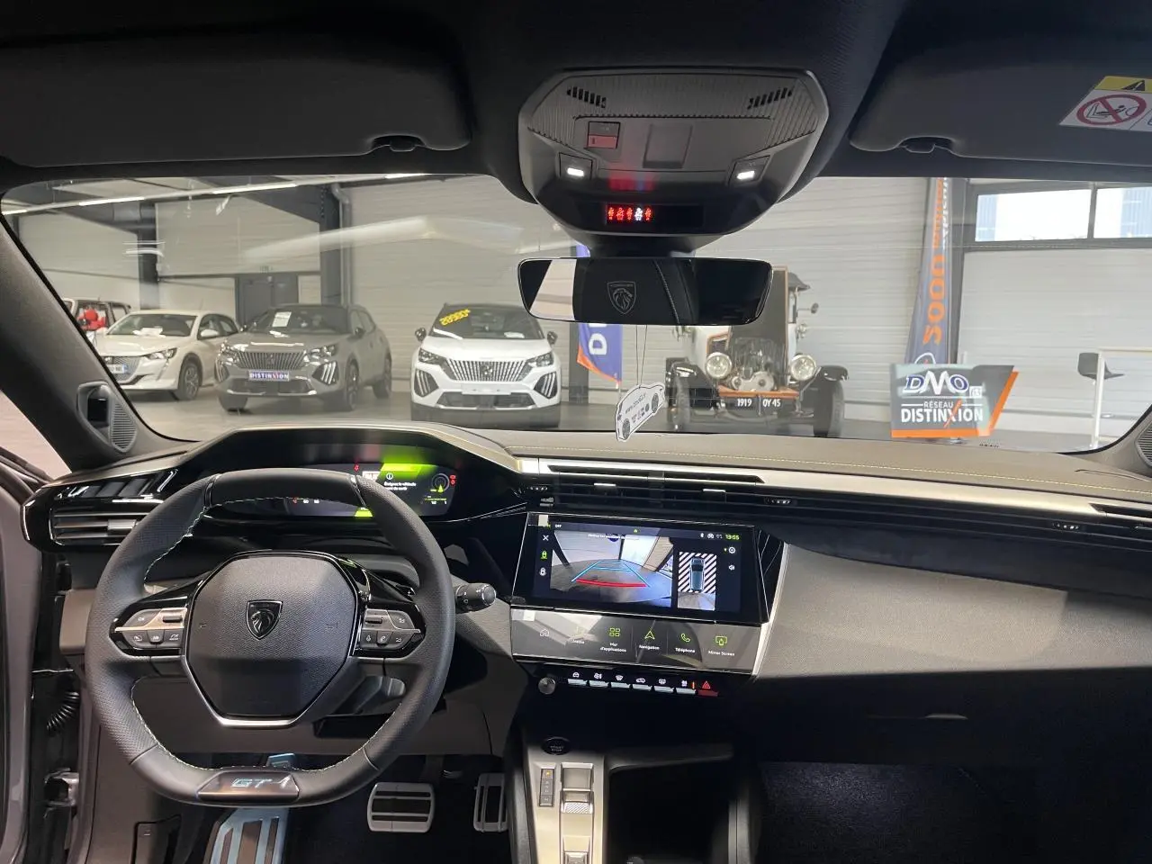 Vue intérieure avant de la Peugeot 308 GT 2026 gris Artense, avec tableau de bord numérique et écran tactile central allumé.