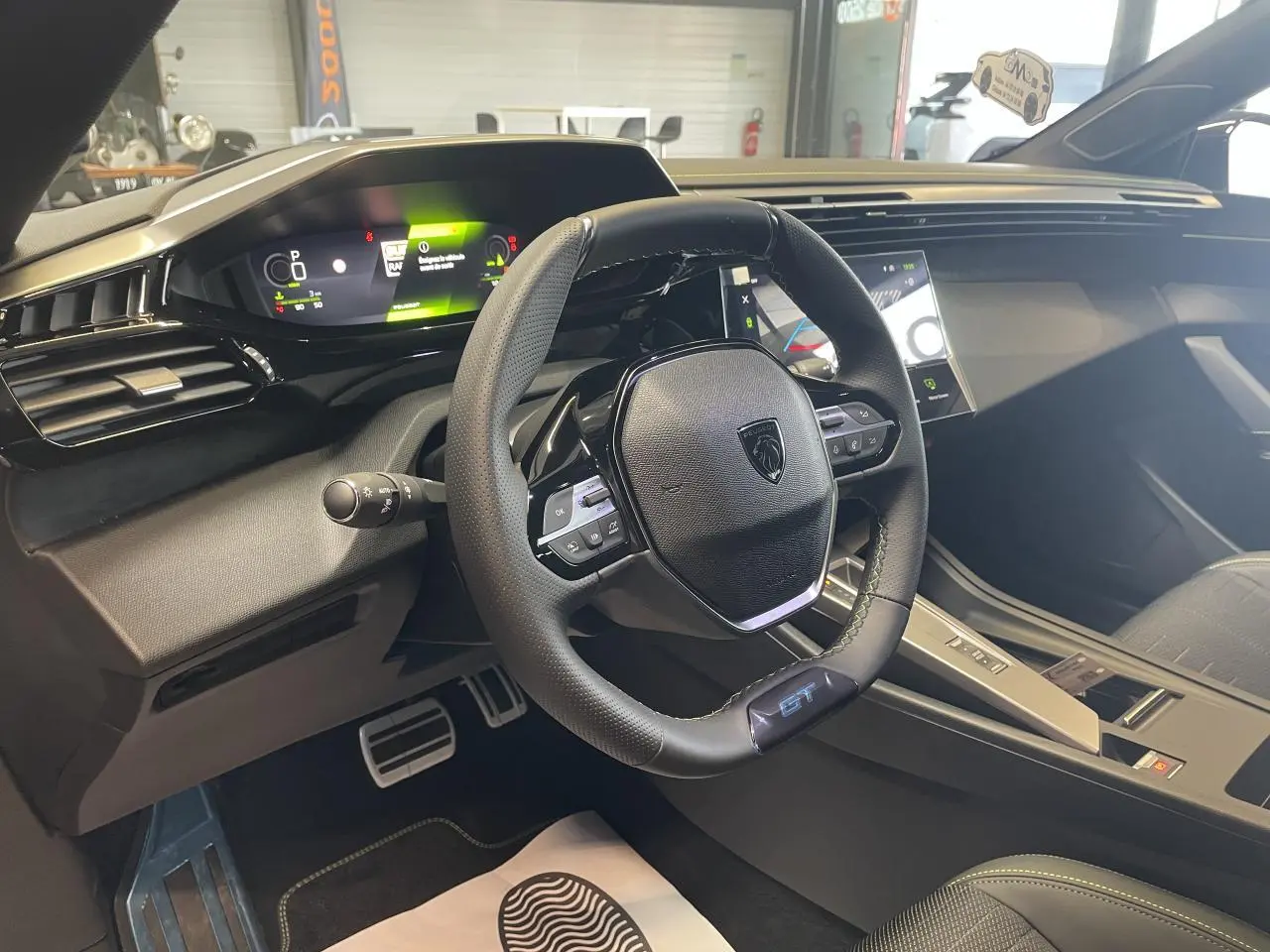 Vue intérieure du poste de conduite Peugeot 308 GT 2026, volant cuir noir avec logo GT et tableau de bord numérique.