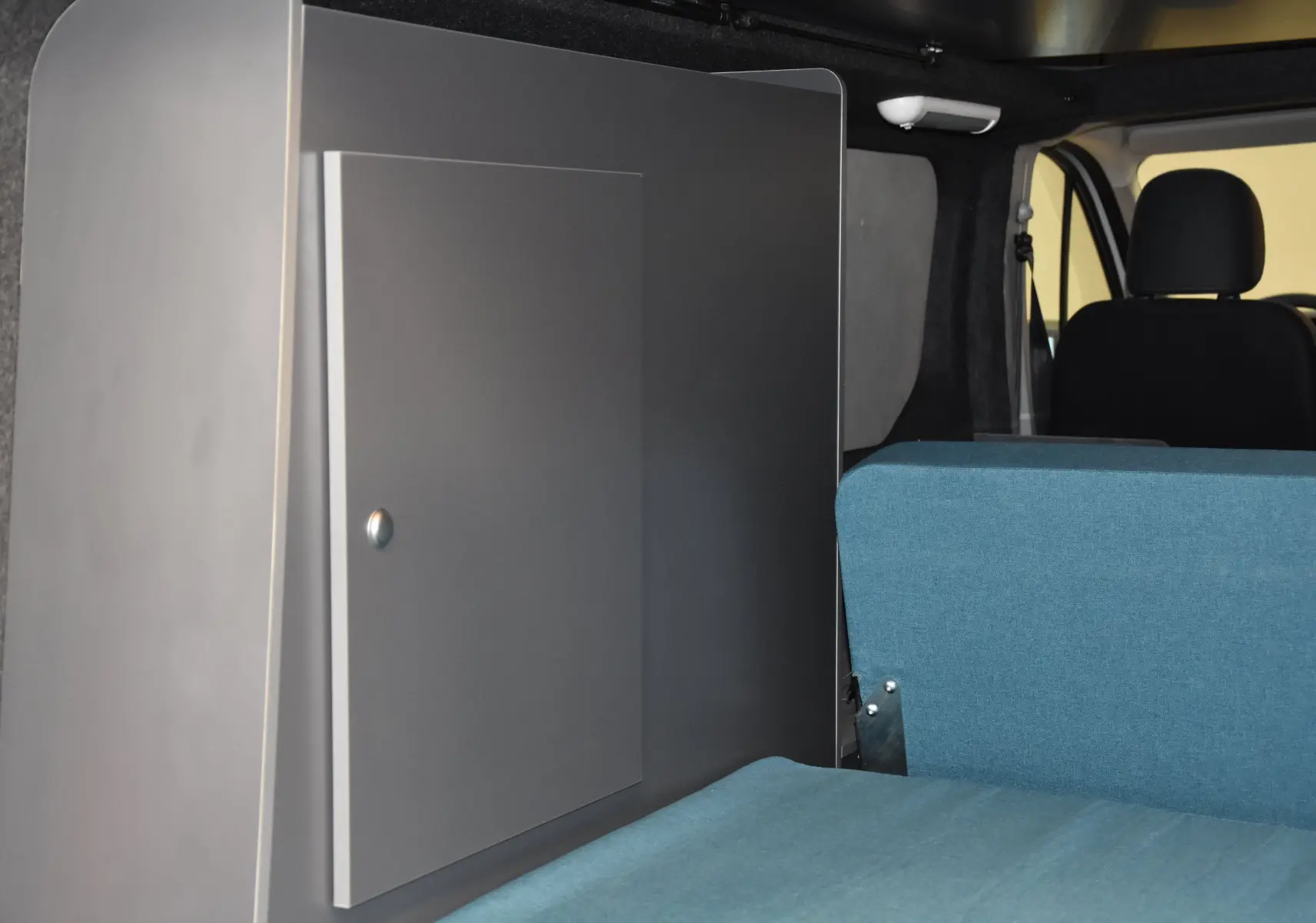 Intérieur du Renault Trafic Combi 2021 montrant un meuble gris et une banquette bleue côté droit, avec sièges avant noirs.
