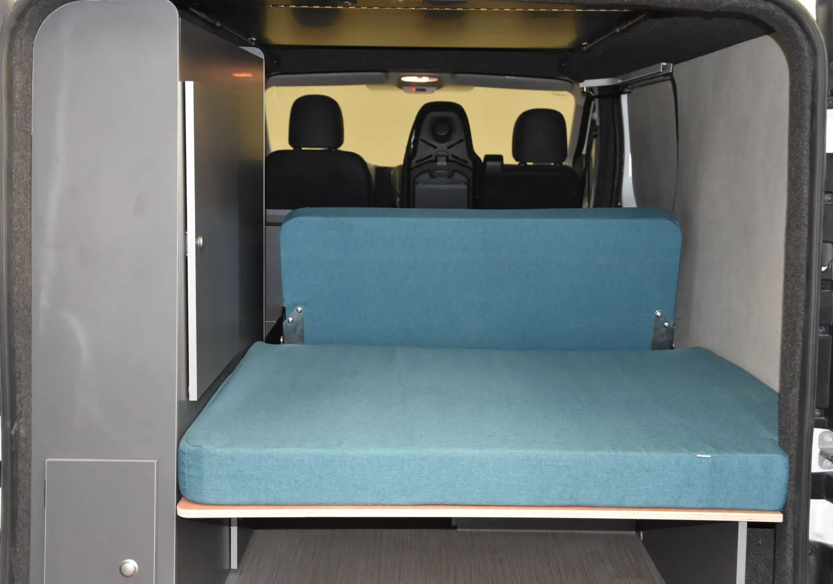 Vue arrière intérieure du Renault Trafic Combi blanc 2021 aménagé avec un lit bleu et un meuble gris.