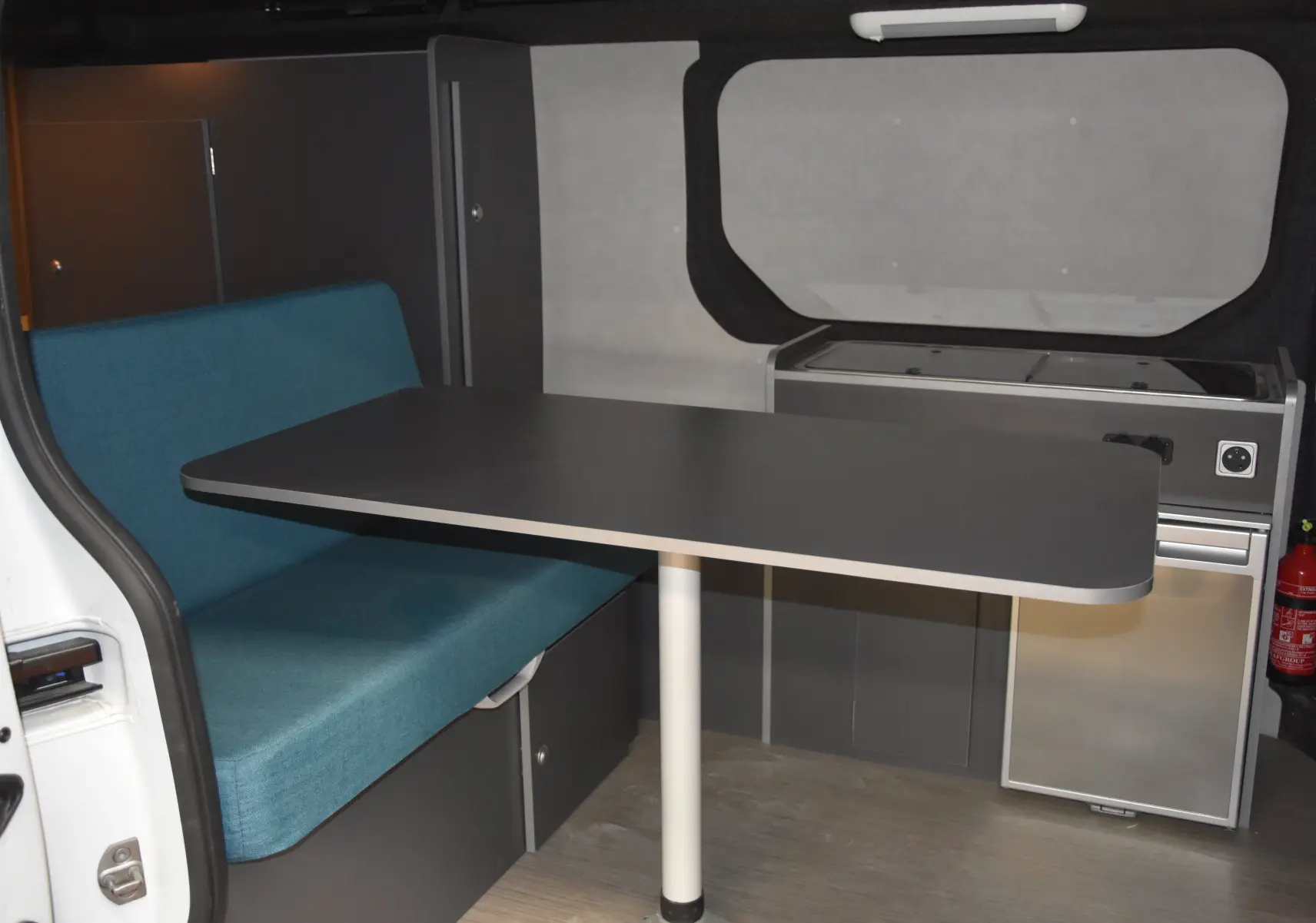 Vue intérieure du Renault Trafic Combi 2.0 DCI 120 L2H1 blanc, avec banquette bleue et table noire centrale.