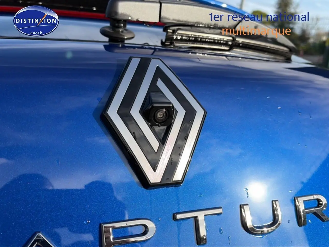 Gros plan sur le logo Renault et la calandre d’un Captur bleu iron 2025 avec caméra de recul intégrée.