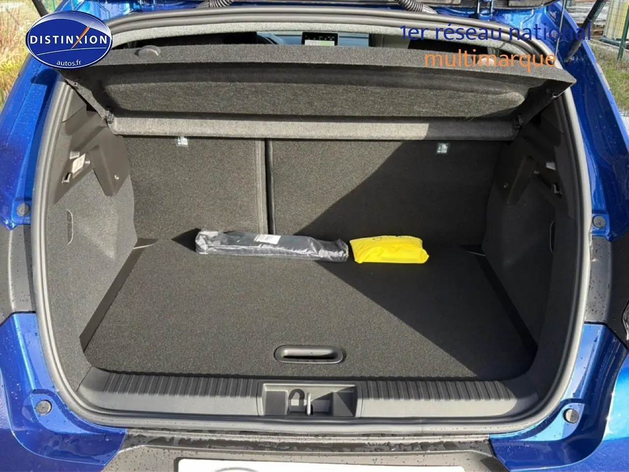 Coffre ouvert d'un Renault Captur Bleu Iron 2025, montrant un espace de rangement propre avec deux objets posés.