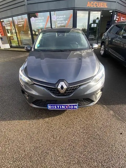 Vue avant d'une Renault Clio gris métallisé 2021, avec logo distinctif et plaque "DISTINXION" visible devant un bâtiment.