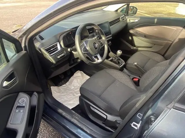 Vue intérieure côté conducteur de la Renault Clio gris 2021, montrant le volant, la boîte manuelle et les sièges tissu gris.
