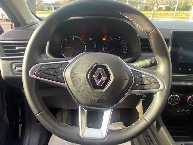 Vue rapprochée du volant en cuir noir de la Renault Clio 1.5 dCi 2021 avec commandes intégrées et tableau de bord allumé.