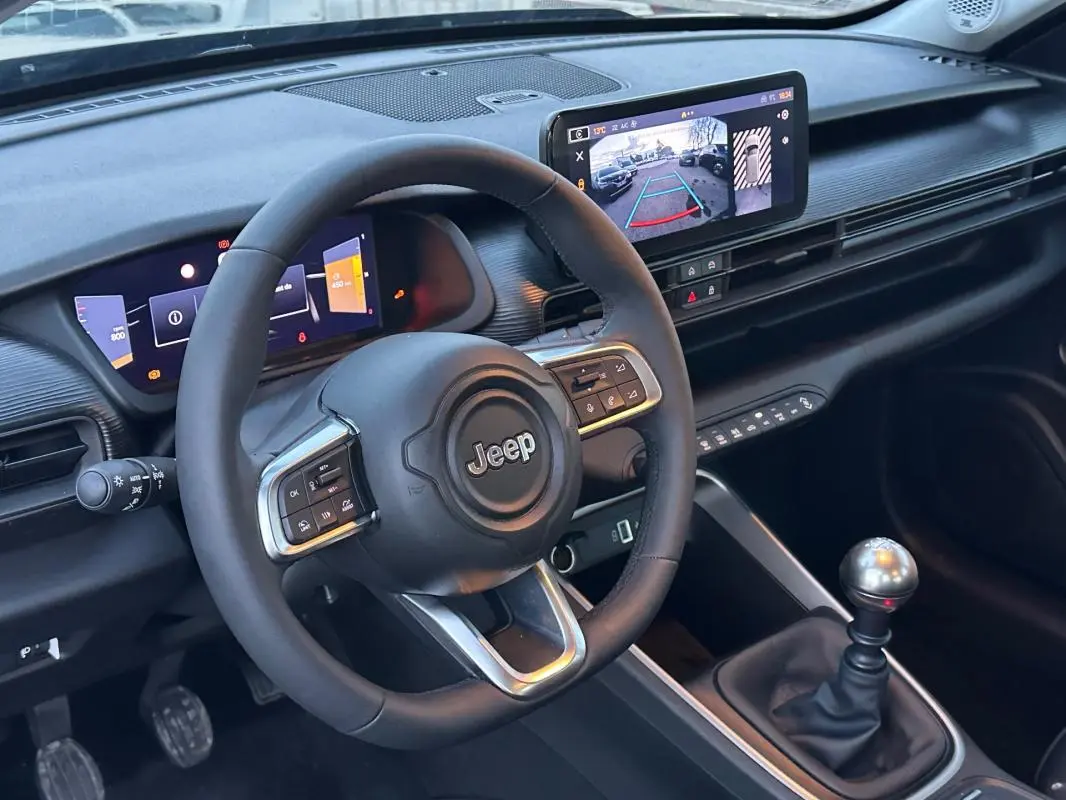 Vue intérieure centrée sur le volant Jeep et la console avec levier de vitesse manuelle et écran multimédia affichant la caméra de recul.