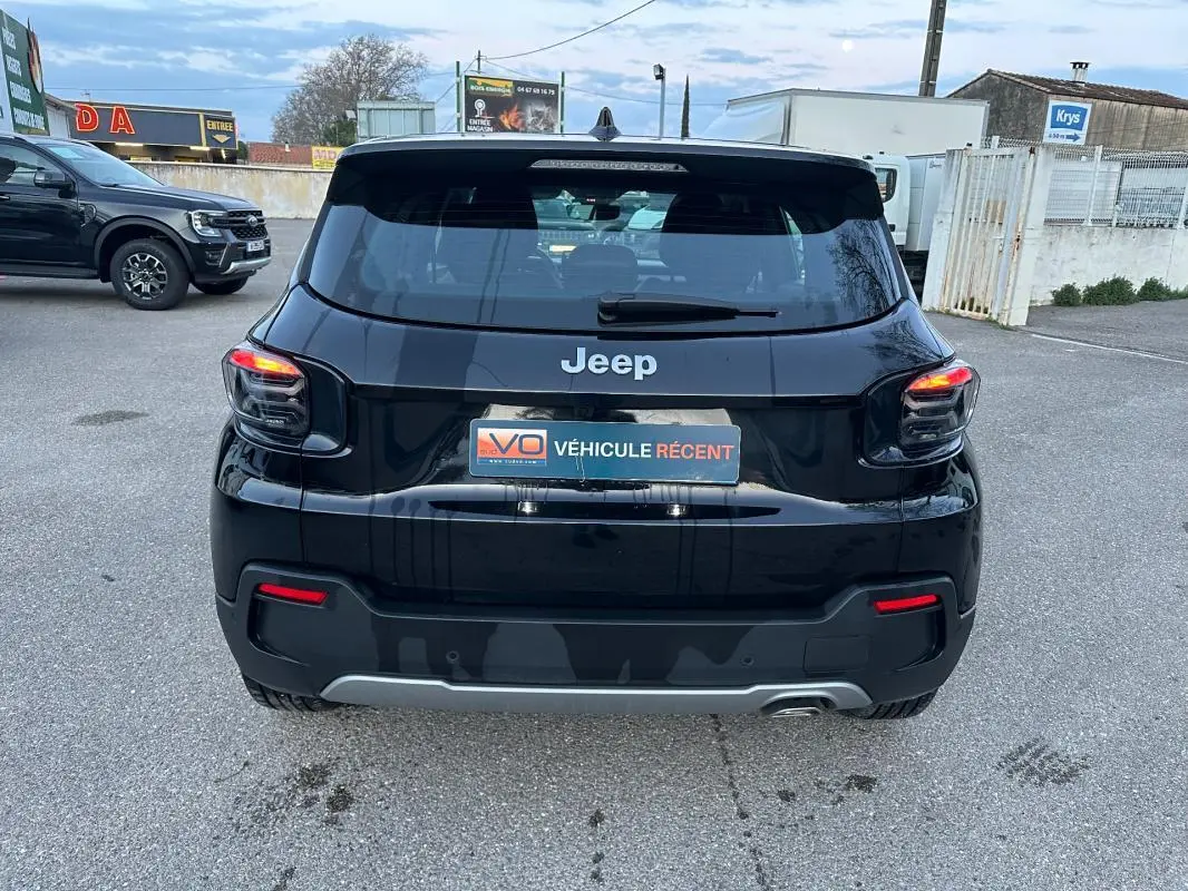 Vue arrière d'un Jeep Avenger noir 2025 avec feux allumés et plaque "Véhicule récent" sur parking extérieur.