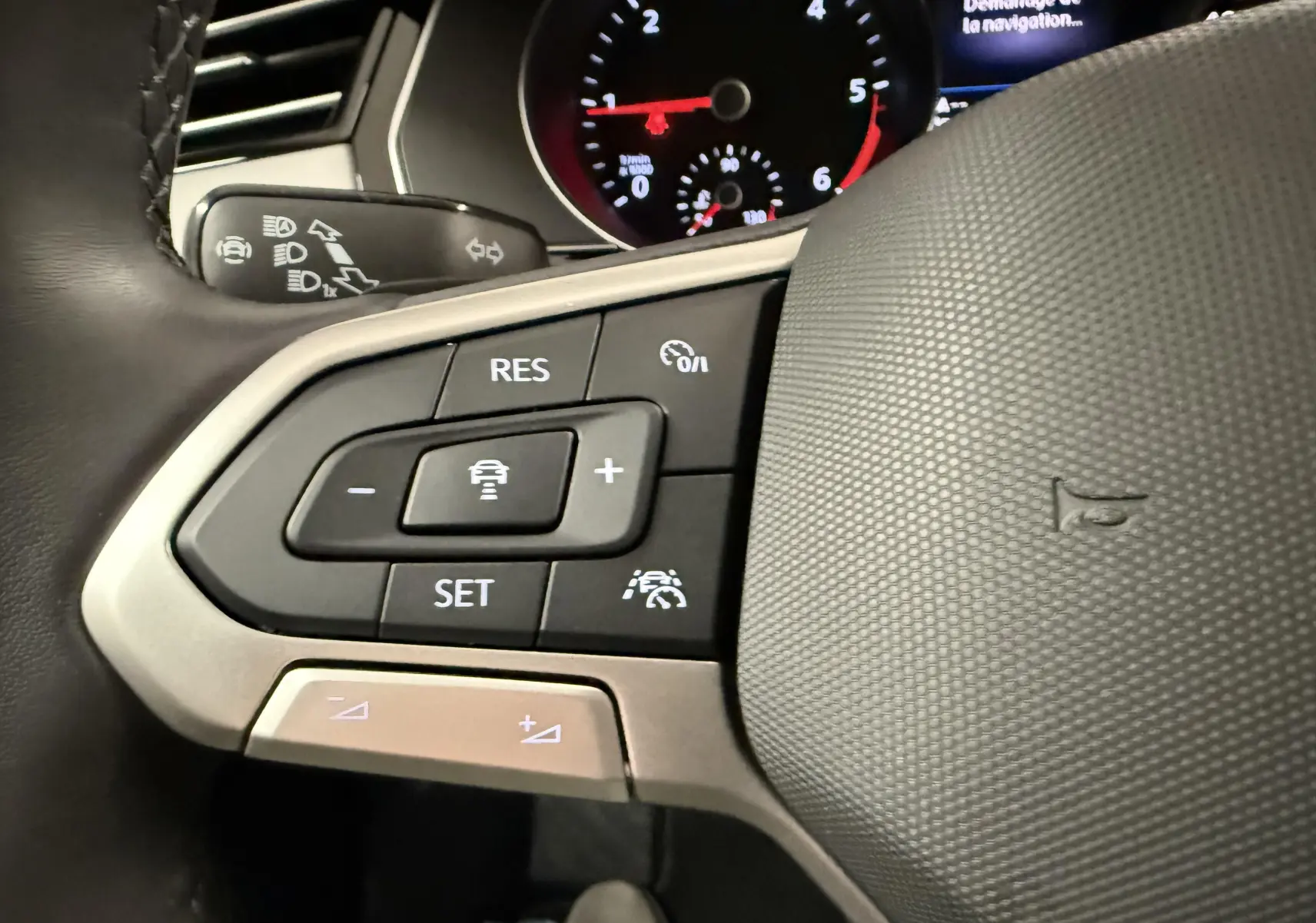 Gros plan sur les commandes à gauche du volant gris texturé d'une Volkswagen Passat SW 2.0 TDI 122 DSG7 Business 2024.