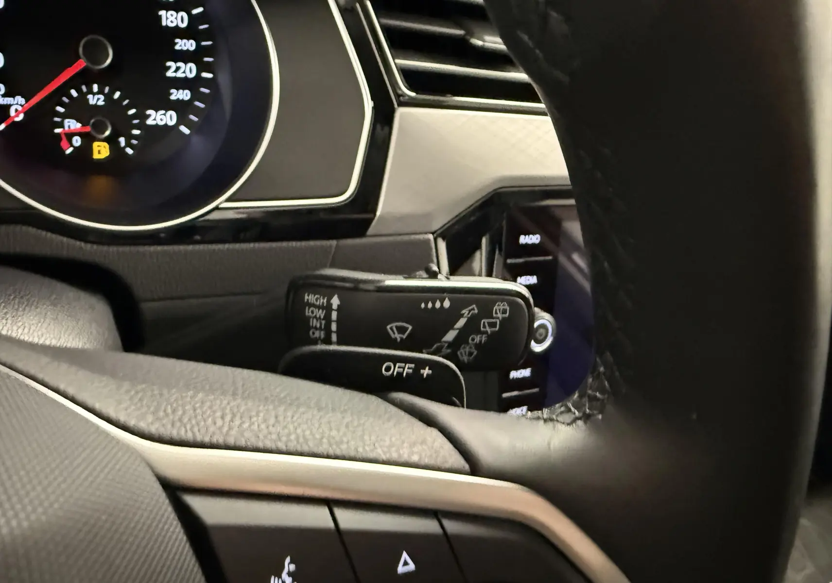 Gros plan sur la commande d’essuie-glace à gauche du volant dans l’habitacle gris et noir de la Volkswagen Passat SW 2024.