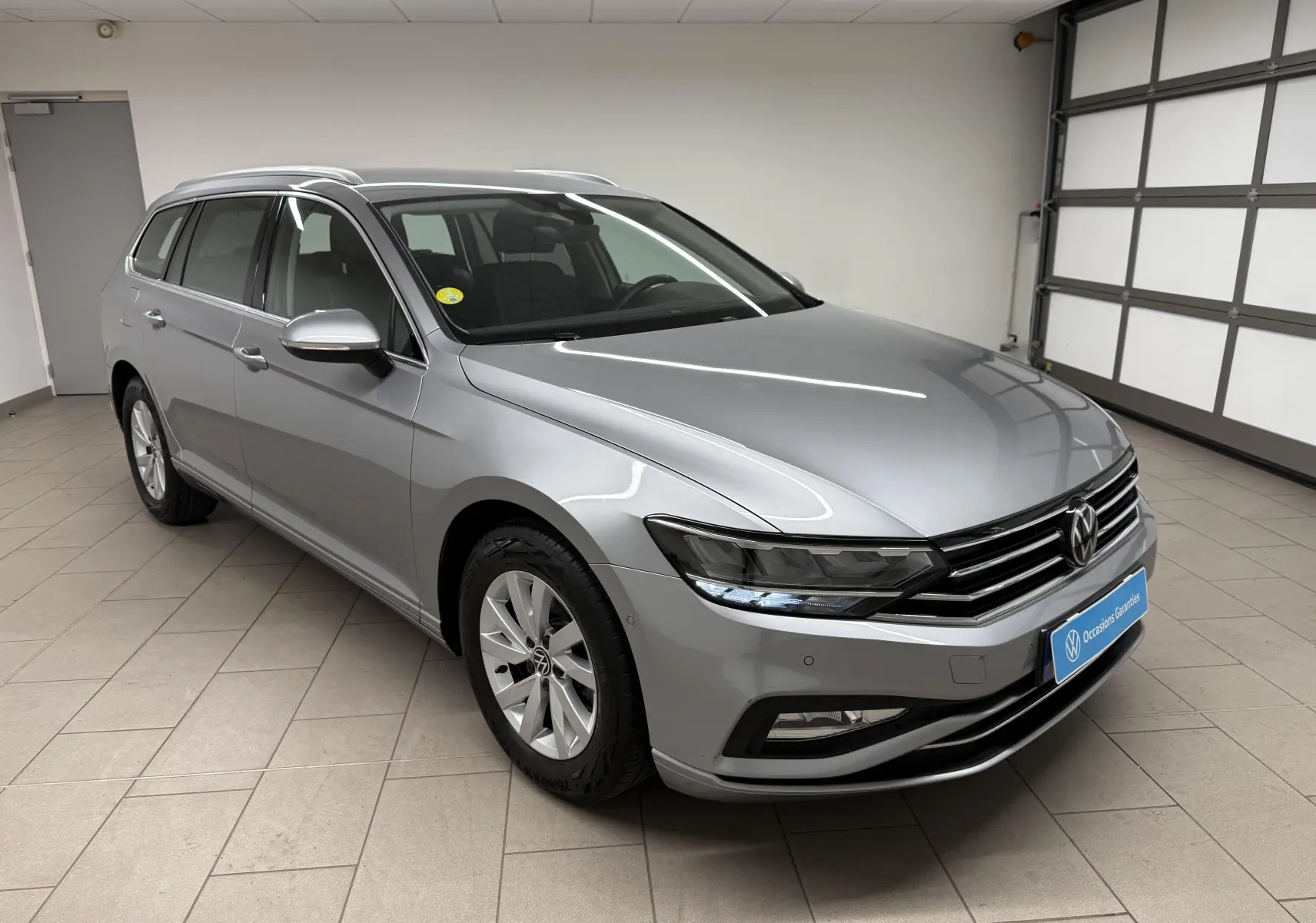 Vue 3/4 avant droite d'une Volkswagen Passat SW 2024 gris pyrite avec calandre chromée et phares LED distinctifs.