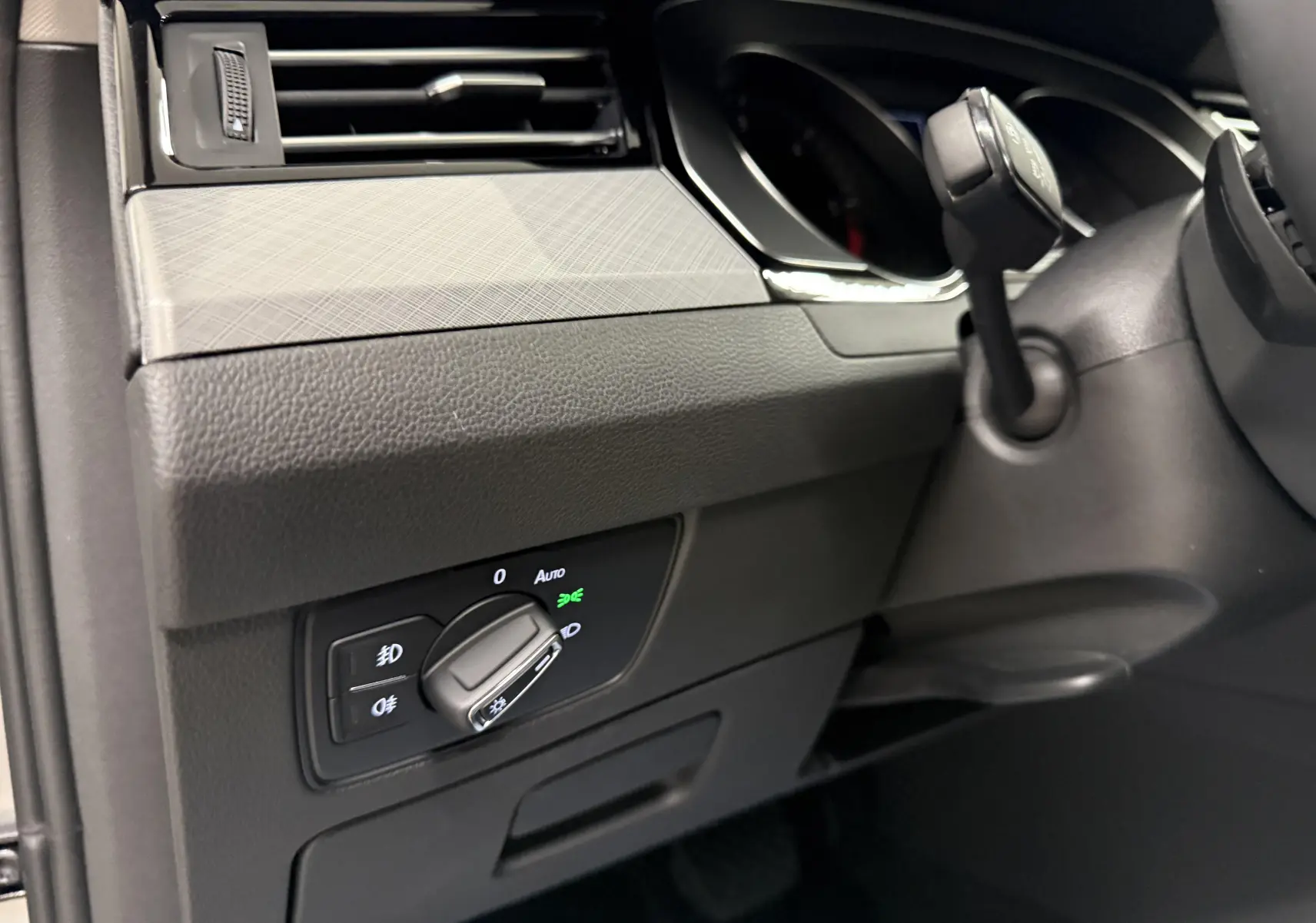 Gros plan sur le bouton de commande des phares à gauche du volant dans l’habitacle gris d’une Volkswagen Passat SW 2024.