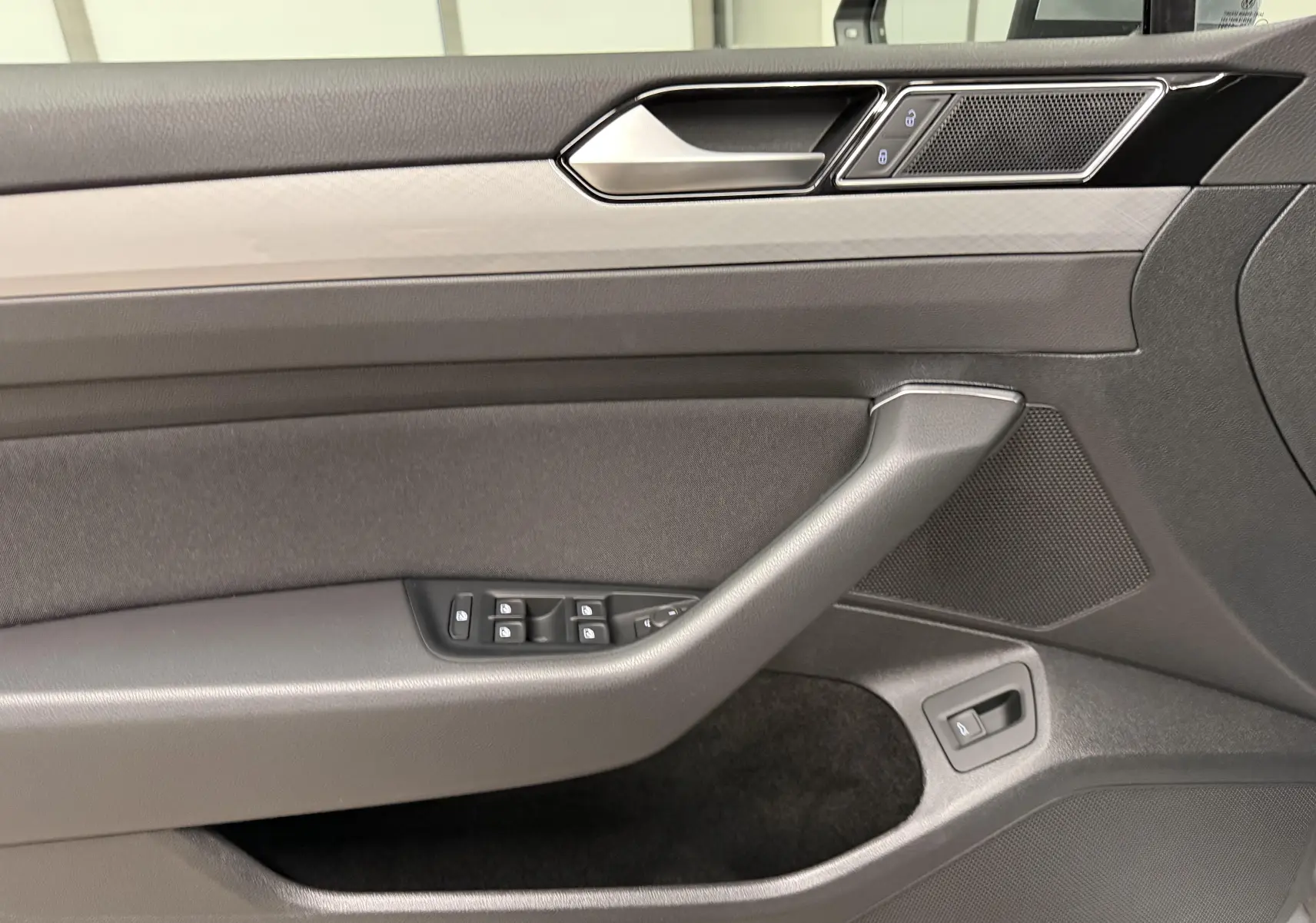 Vue intérieure côté gauche de la porte d'une Volkswagen Passat SW 2024 avec commandes de vitres et finition sobre.