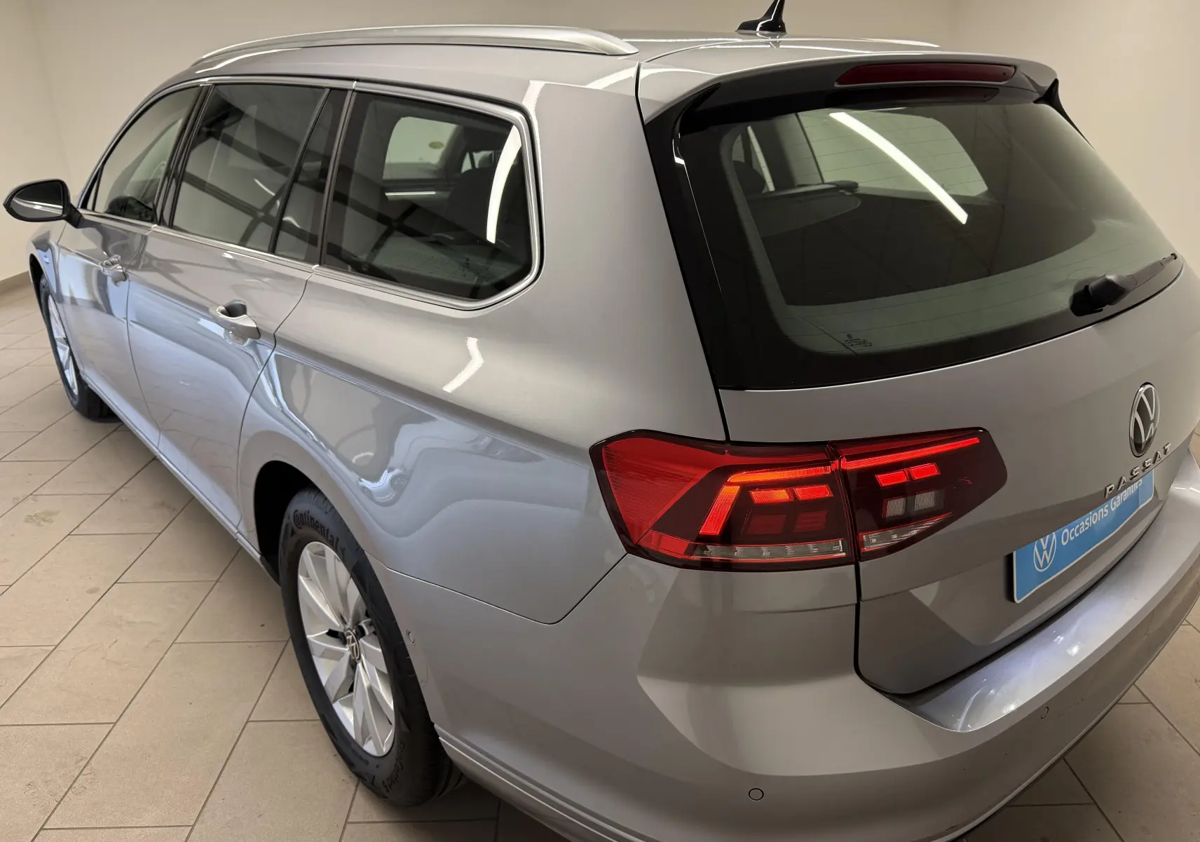 Vue 3/4 arrière droite d'une Volkswagen Passat SW 2.0 TDI 122 DSG7 Business gris pyrite métallisé avec feux arrière allumés.