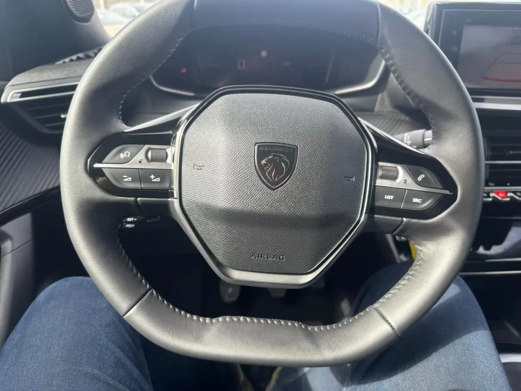 Vue rapprochée du volant cuir noir du Peugeot 2008 2024 avec commandes intégrées et logo central.