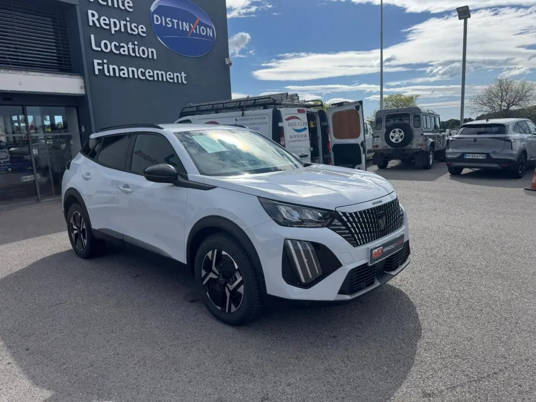 Peugeot 2008 blanc en 3/4 avant droit, avec barres de toit noires et jantes alliage 17 pouces visibles.