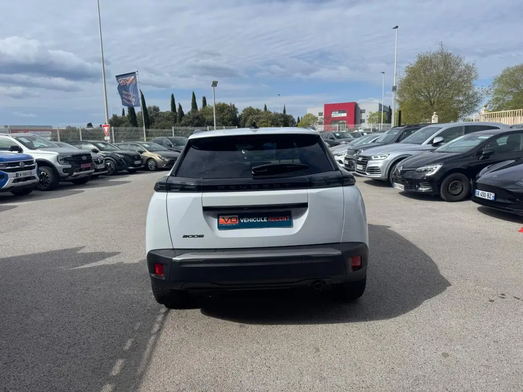 Vue arrière d’un Peugeot 2008 blanc 2024 avec feux noirs et lunette teintée, stationné en extérieur parmi d’autres véhicules.