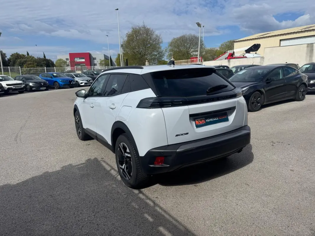 Vue 3/4 arrière droite d’un Peugeot 2008 blanc avec barres de toit et jantes alliage 17 pouces, stationné en extérieur.